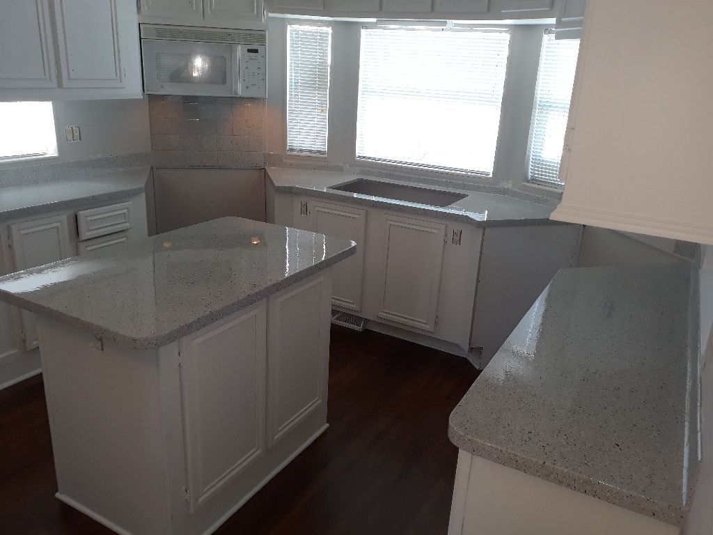 Bright kitchen with white cabinets, speckled countertops, island, and large windows.