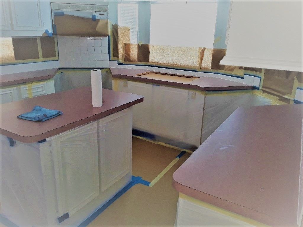 Empty kitchen with white cabinets, pink countertops, and a central island near a window.