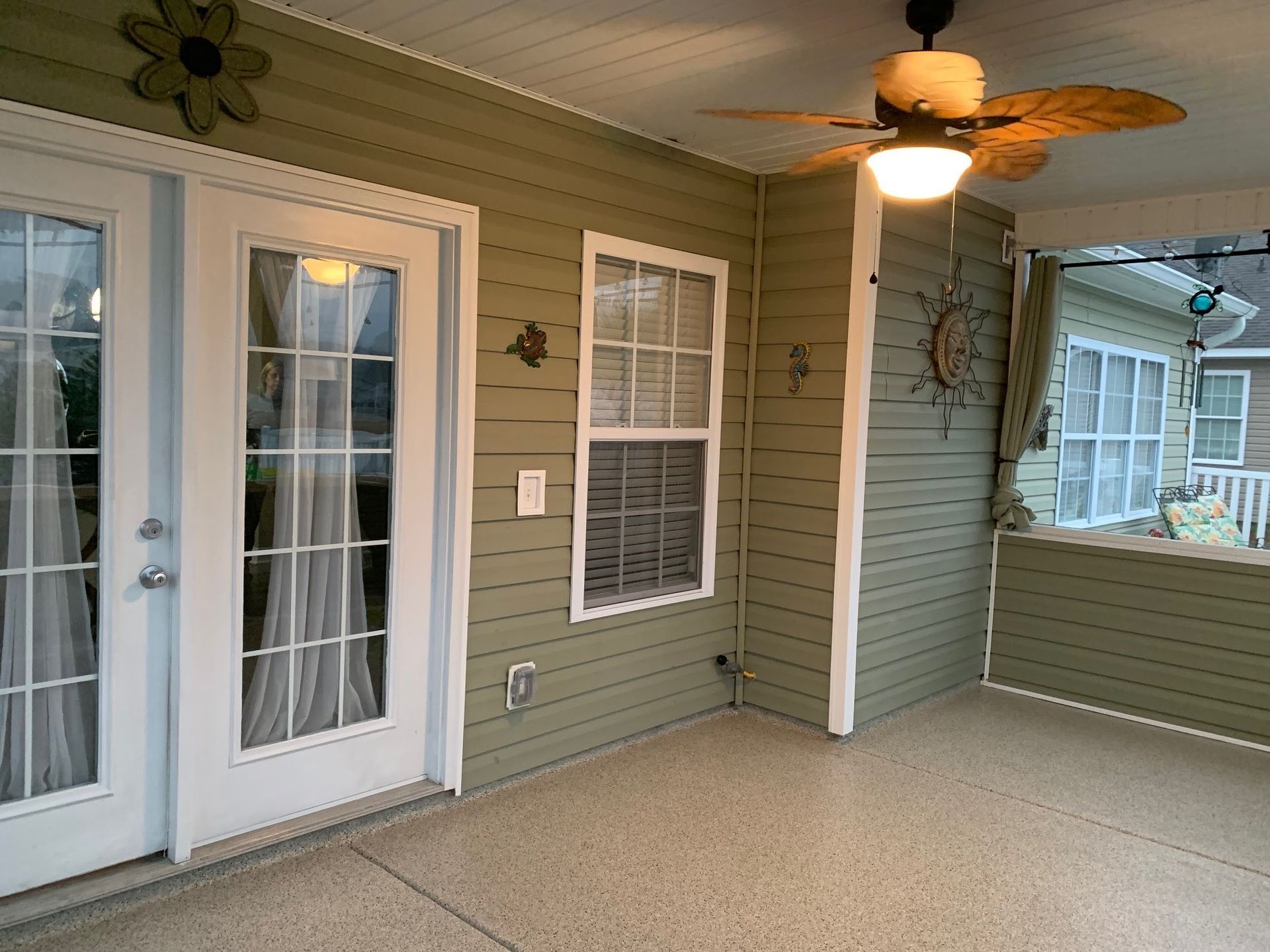 Covered porch with white French doors, ceiling fan, and gray siding.