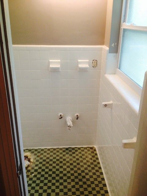 Small bathroom with white tiled walls, checkered floor, and a tub or shower window on the right.