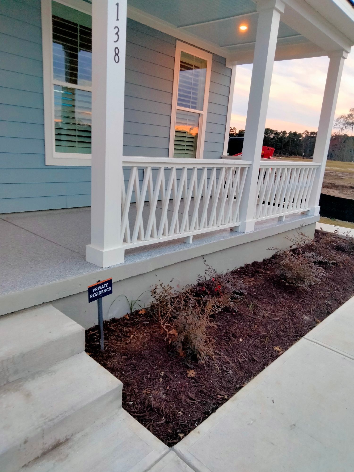 Front porch with white railings and steps beside a mulched planting bed at dusk.
