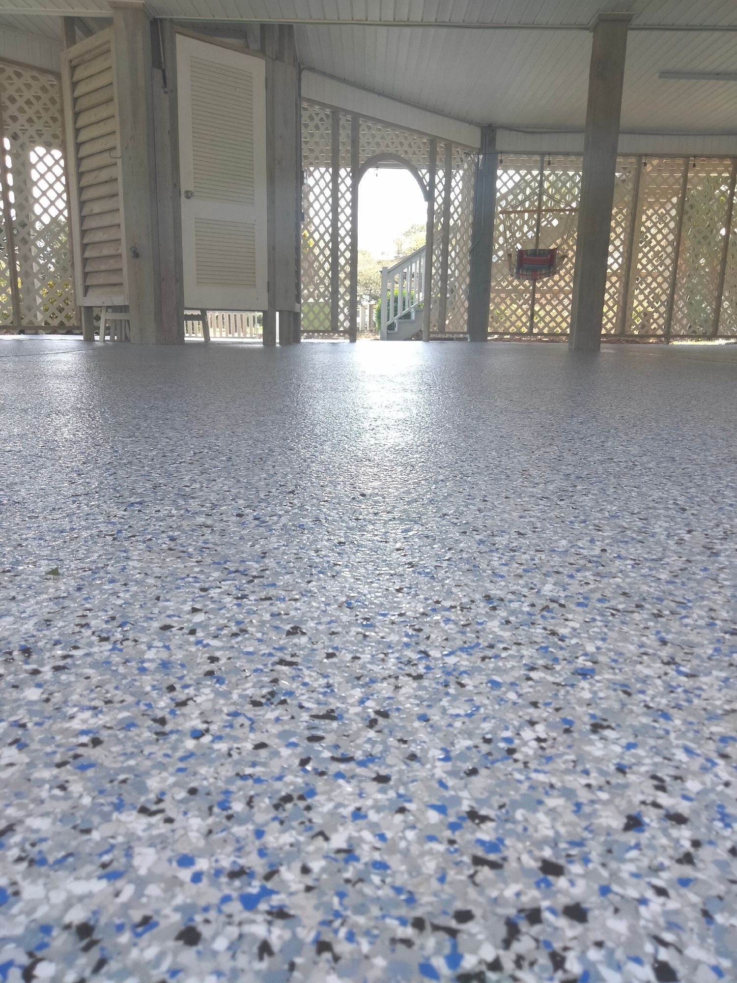 Speckled terrazzo floor under a covered porch with lattice walls and white shutters