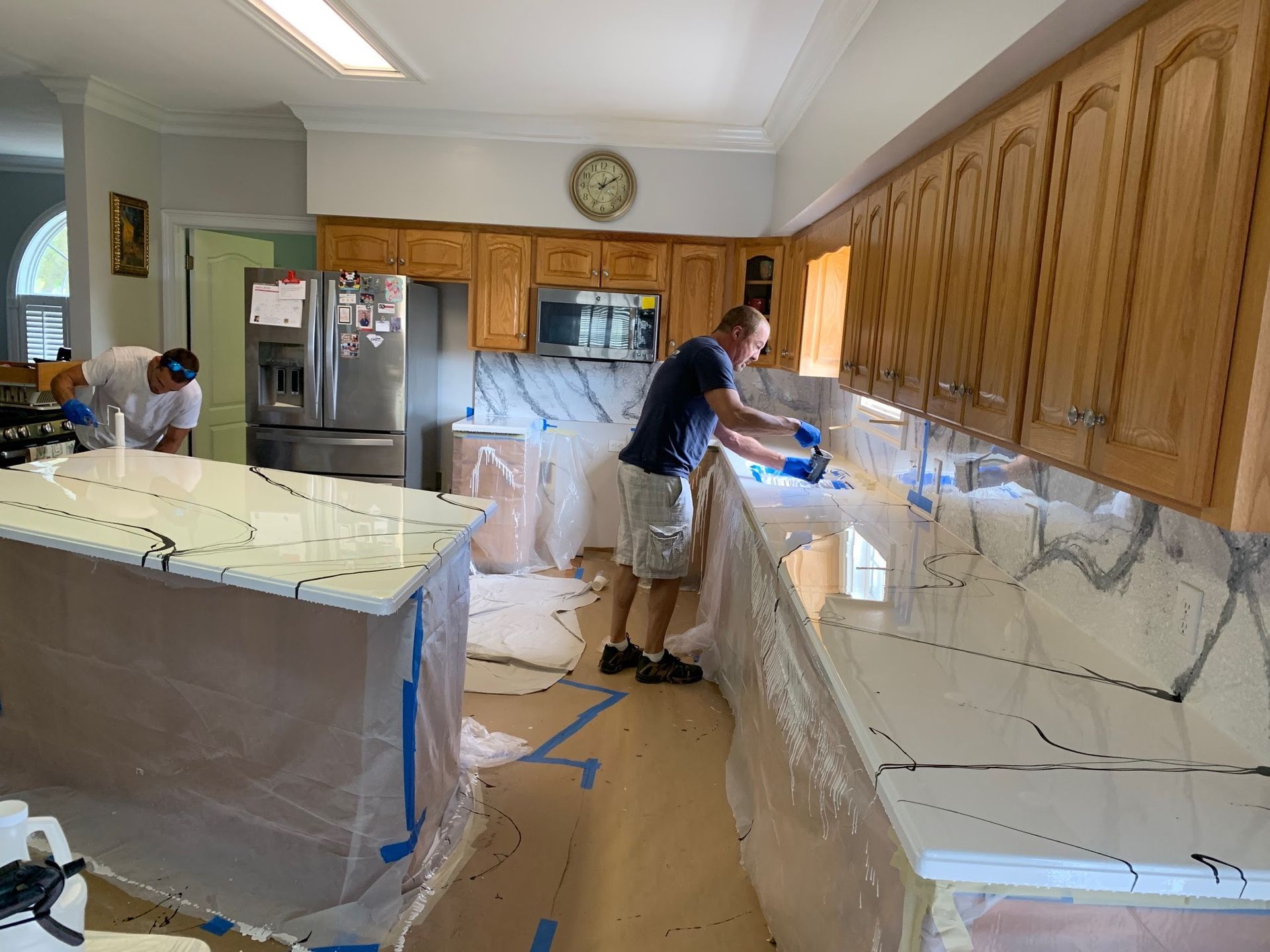 People working on a kitchen renovation, with cabinets and counters covered in protective plastic.