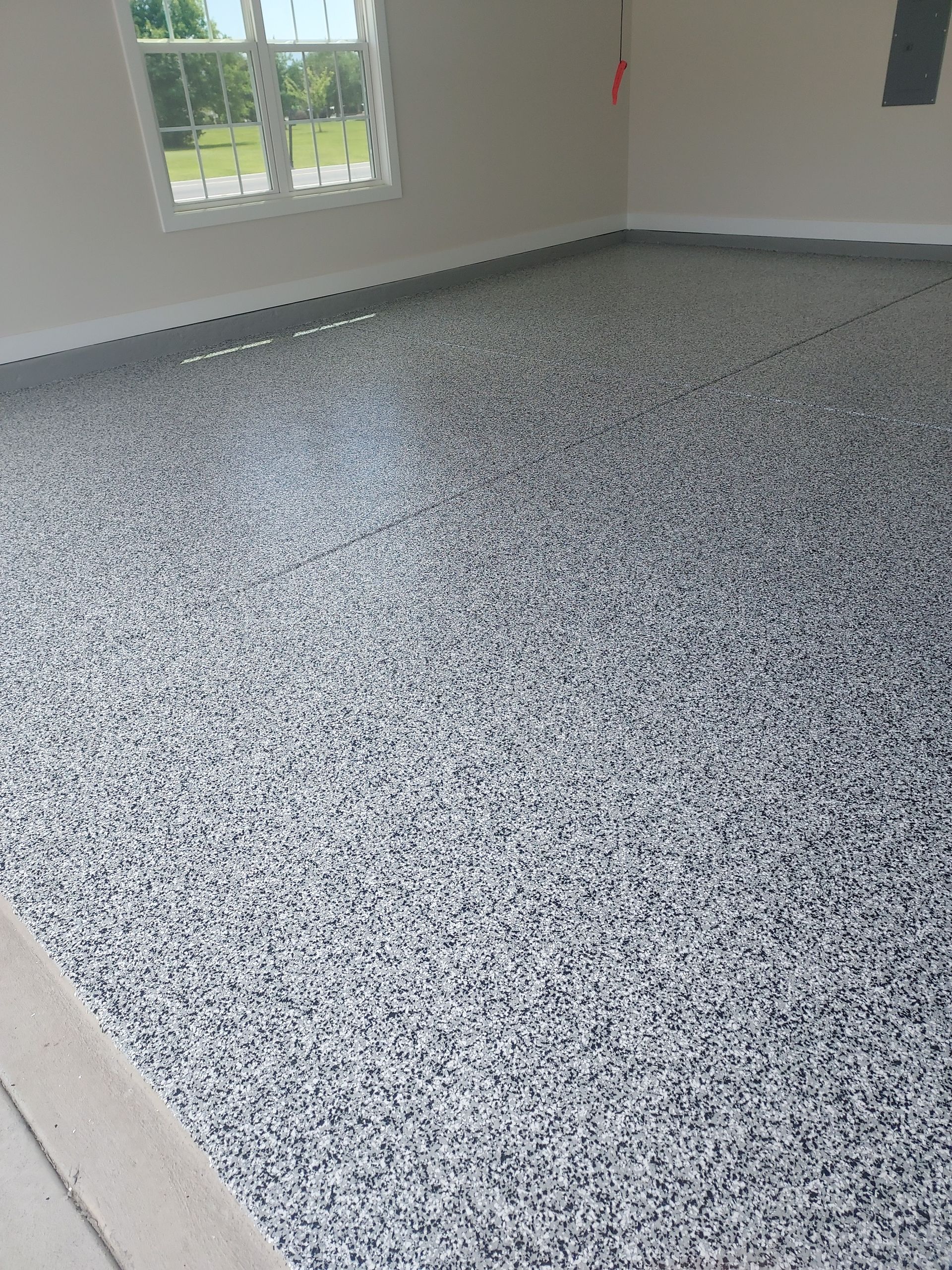 Empty room with speckled epoxy floor, white walls, and a window letting in daylight.