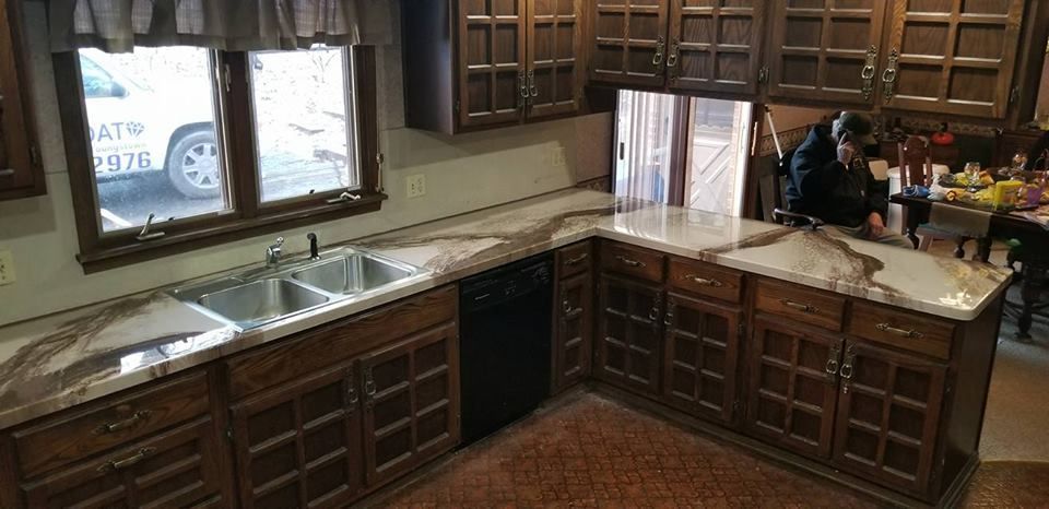 Kitchen with dark wood cabinets, granite countertops, and a person standing by the sink near the window