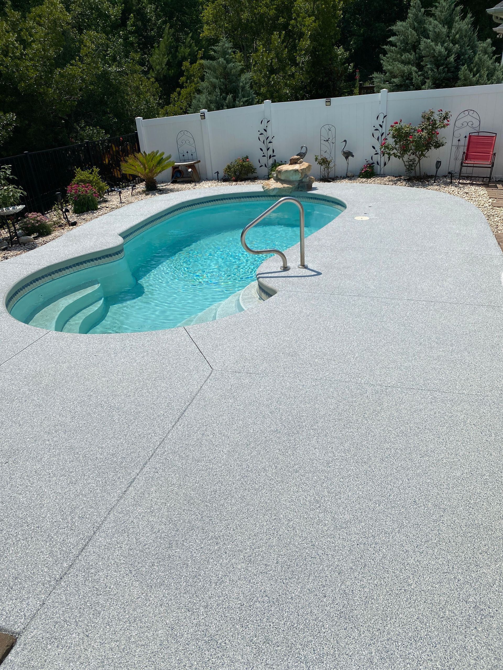 Backyard pool with white gravel deck, metal handrail, and white fence in bright sunlight