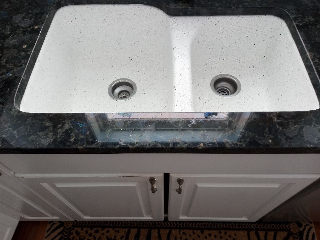 White double-basin kitchen sink with granite countertop and white cabinet doors below.