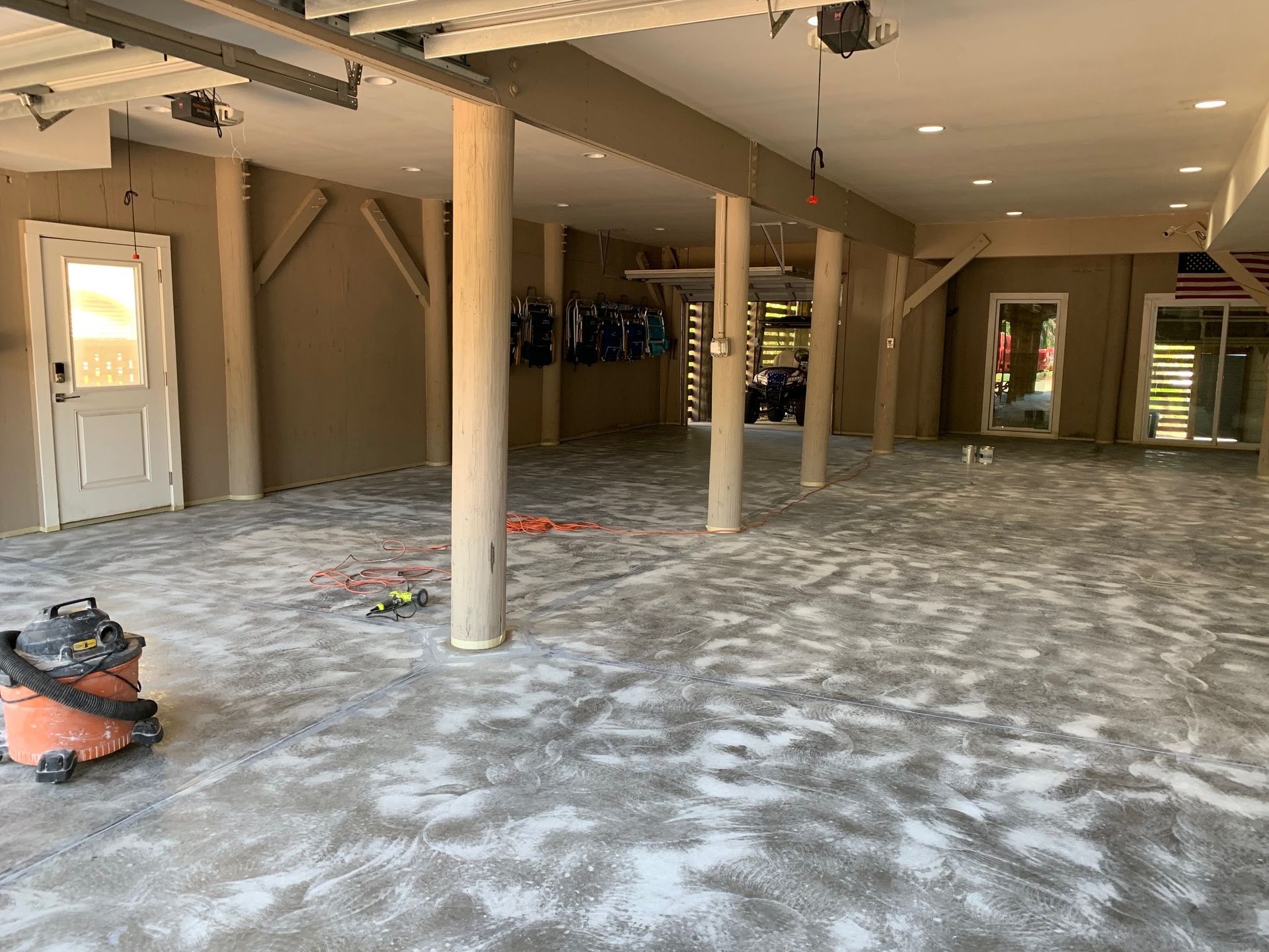 Empty unfinished interior with exposed columns, dust-covered floor, and ceiling lights.