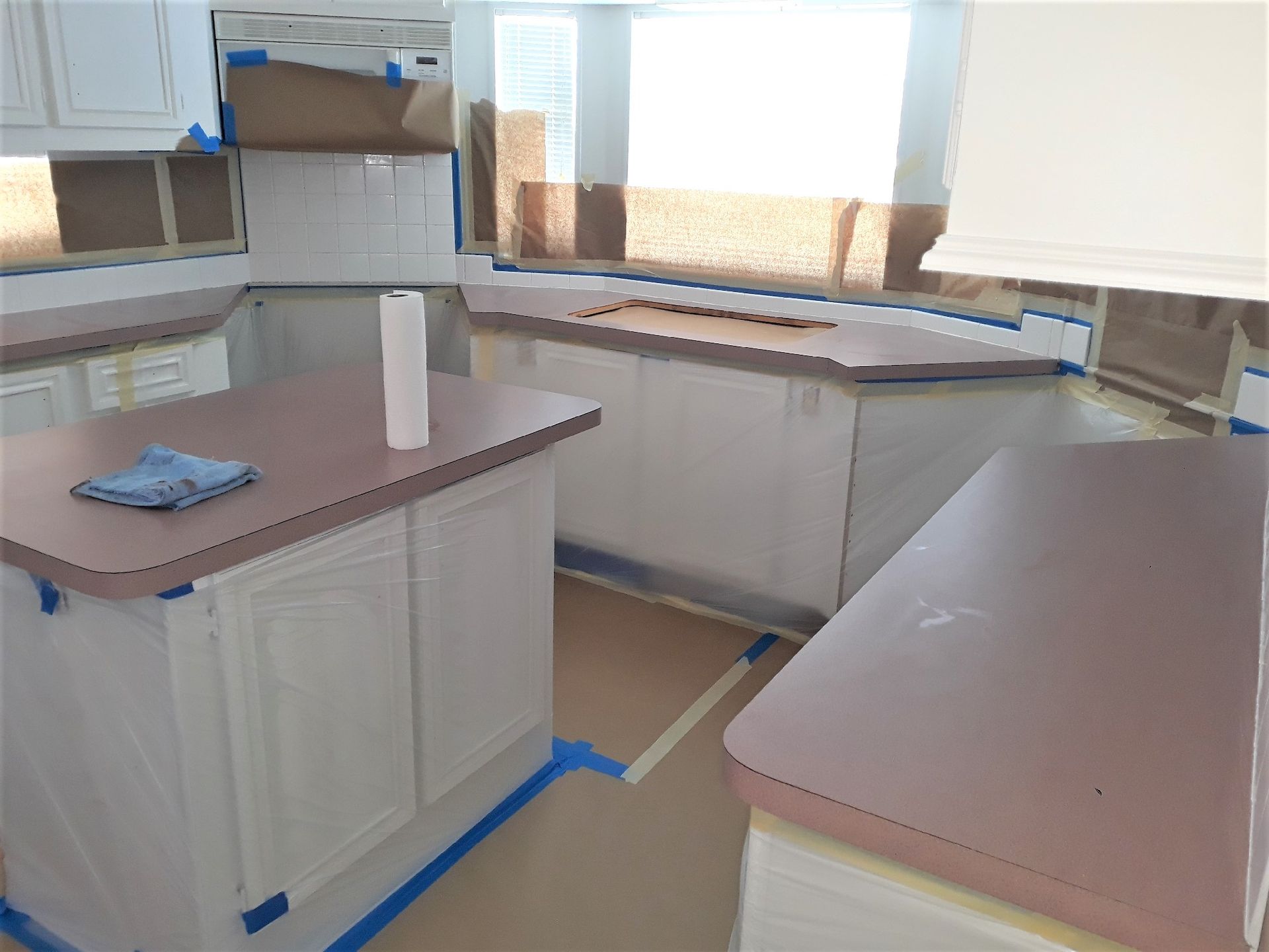 Modern kitchen with white cabinets, beige countertops, and blue painter’s tape along the floor and edges