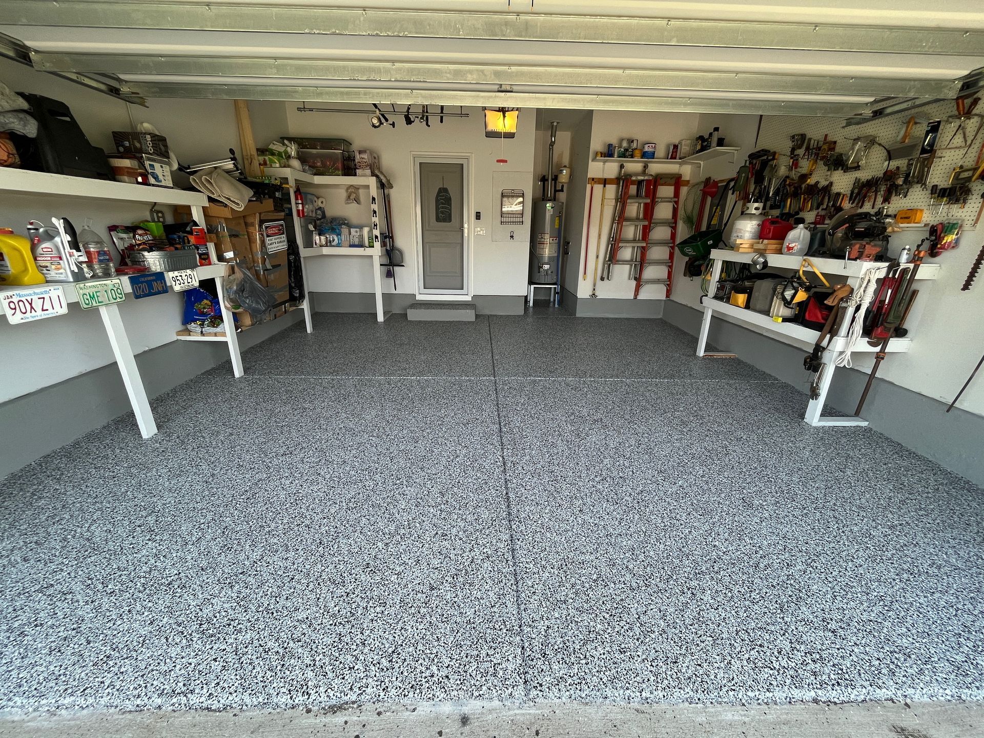Garage interior with open door, gray carpet, shelves, and storage along both walls.