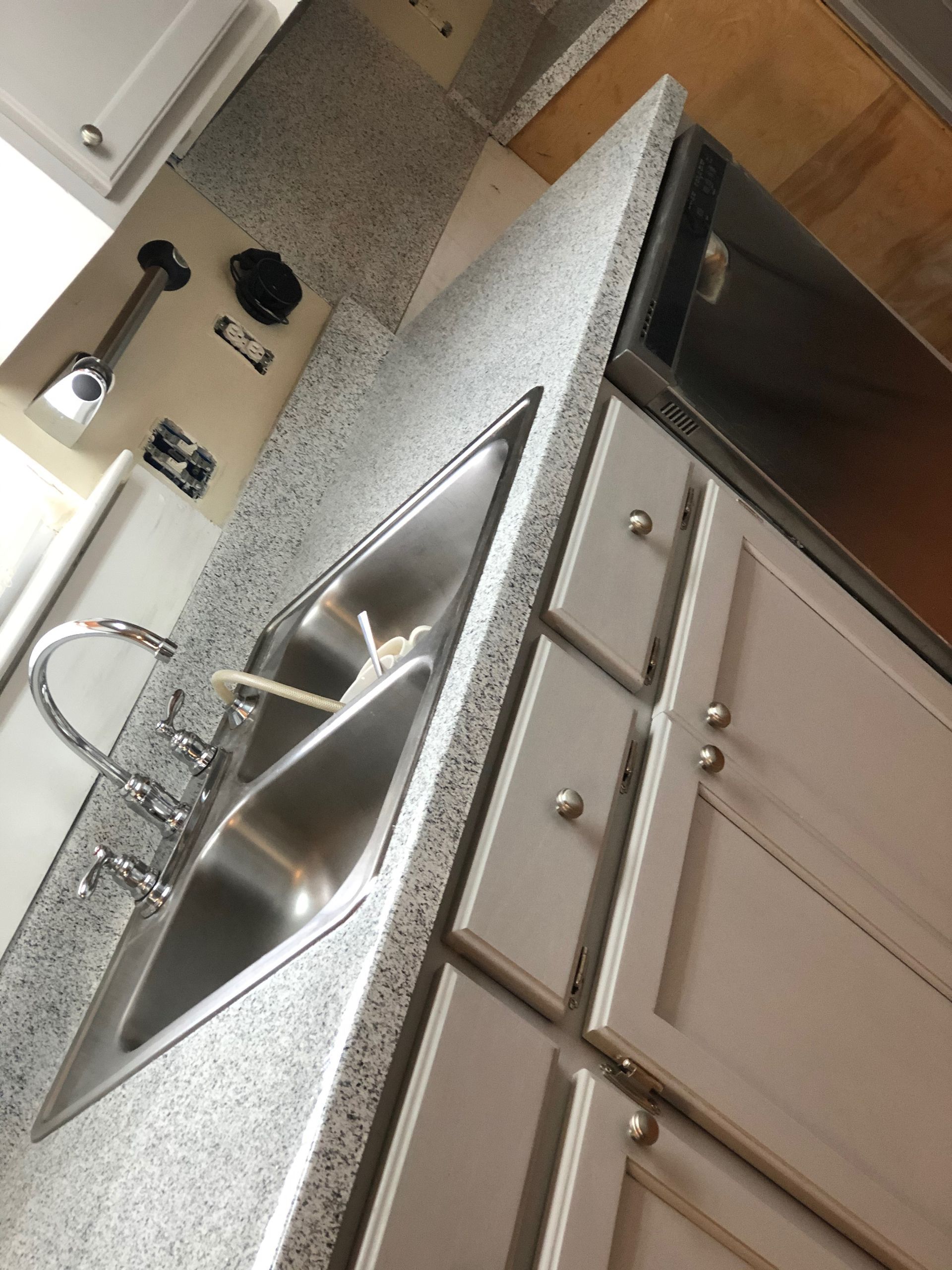 Tilted view of a kitchen sink, granite countertop, and white cabinets, with a dish rack beside the sink