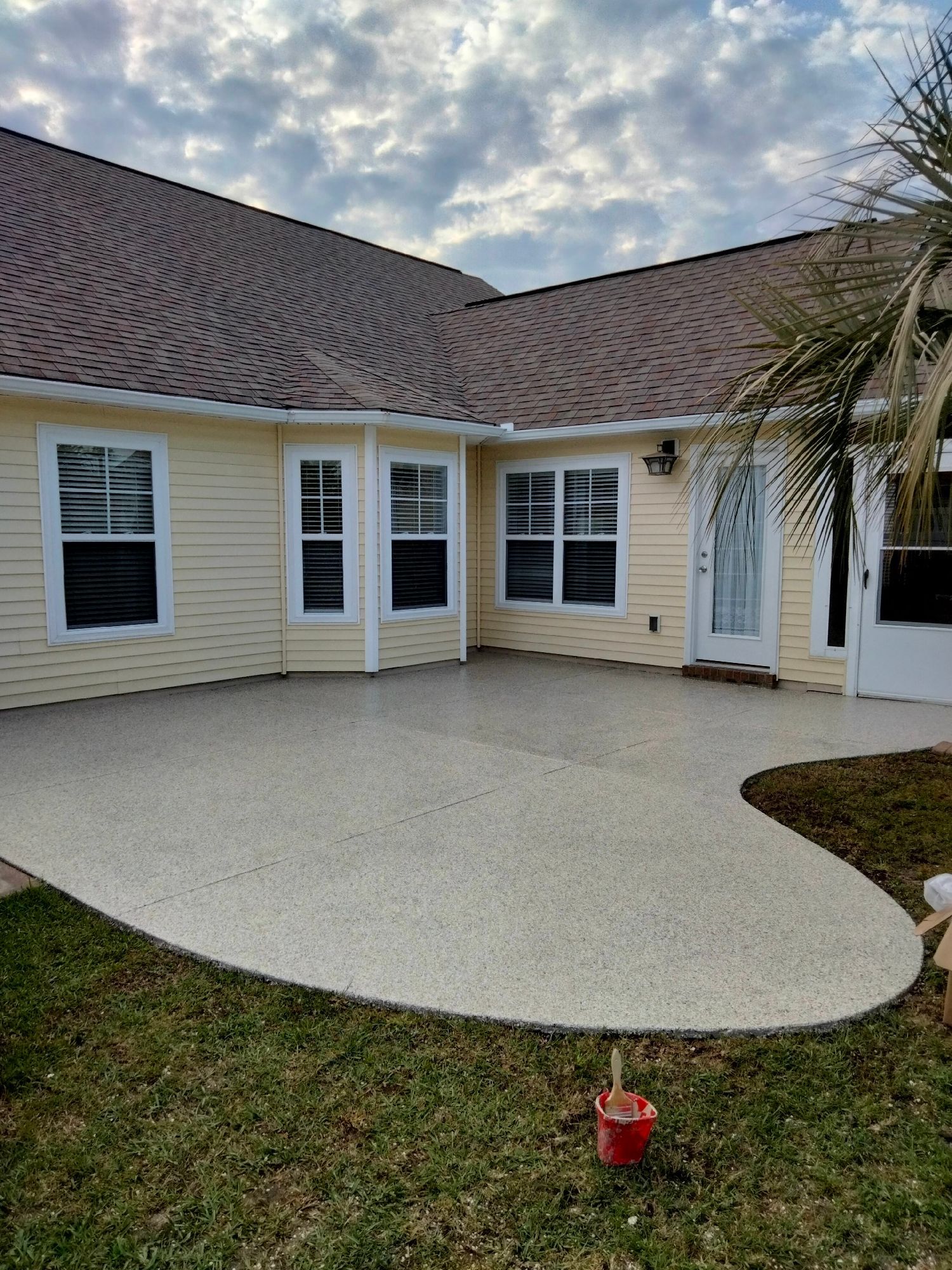 Backyard patio with fresh white concrete, beige house siding, and cloudy sky overhead