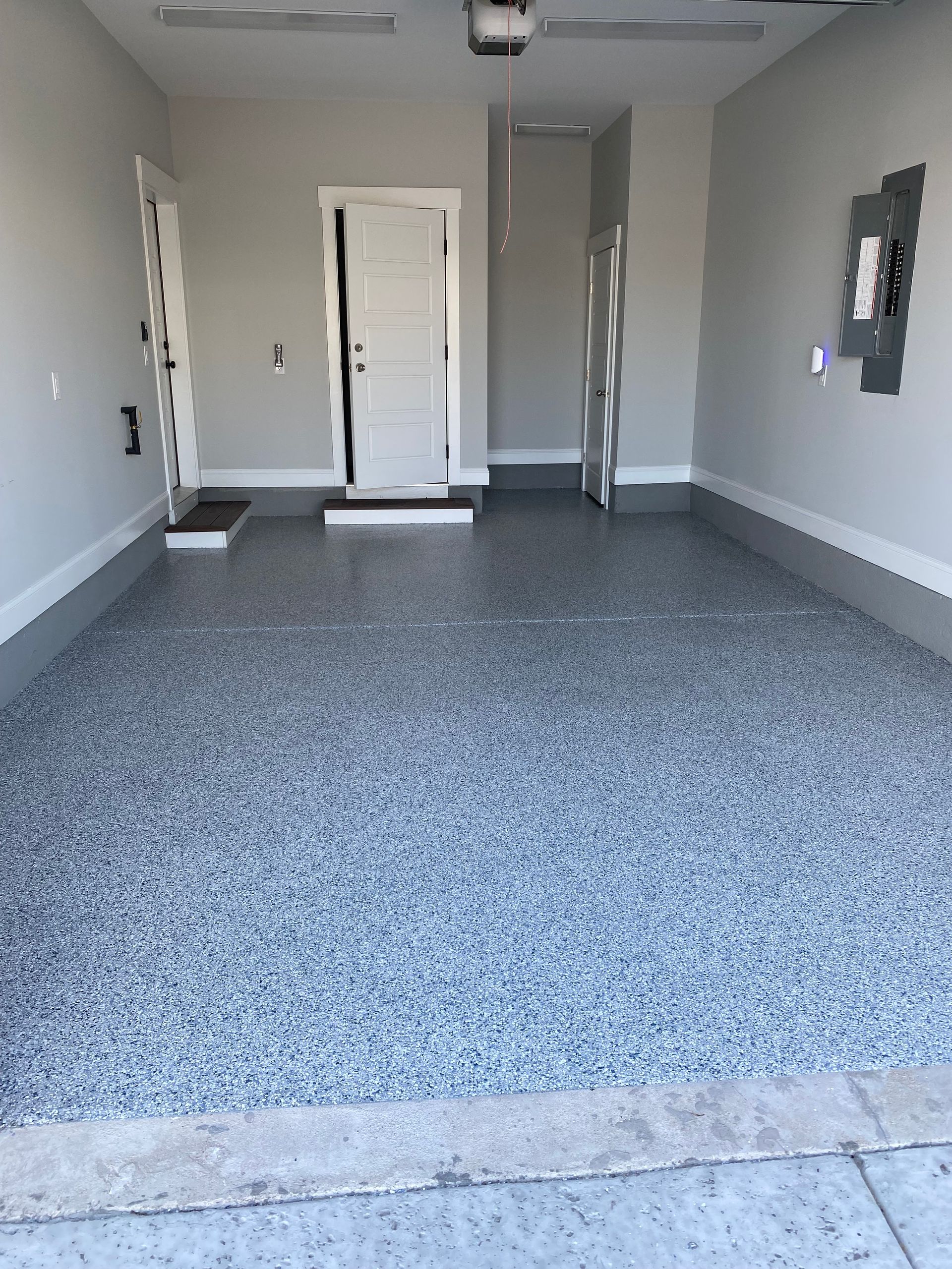 Empty carpeted garage interior with gray walls and a white door at the back
