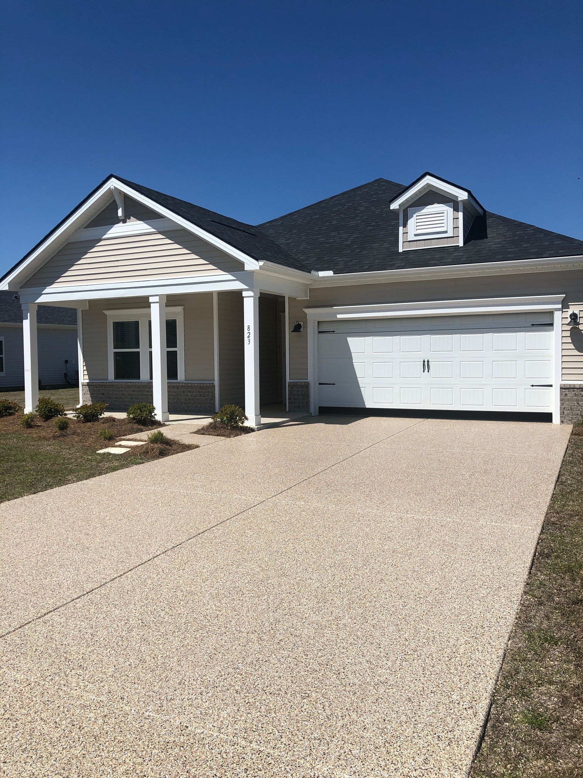 Single-story beige house with a white garage and gravel driveway under a clear blue sky