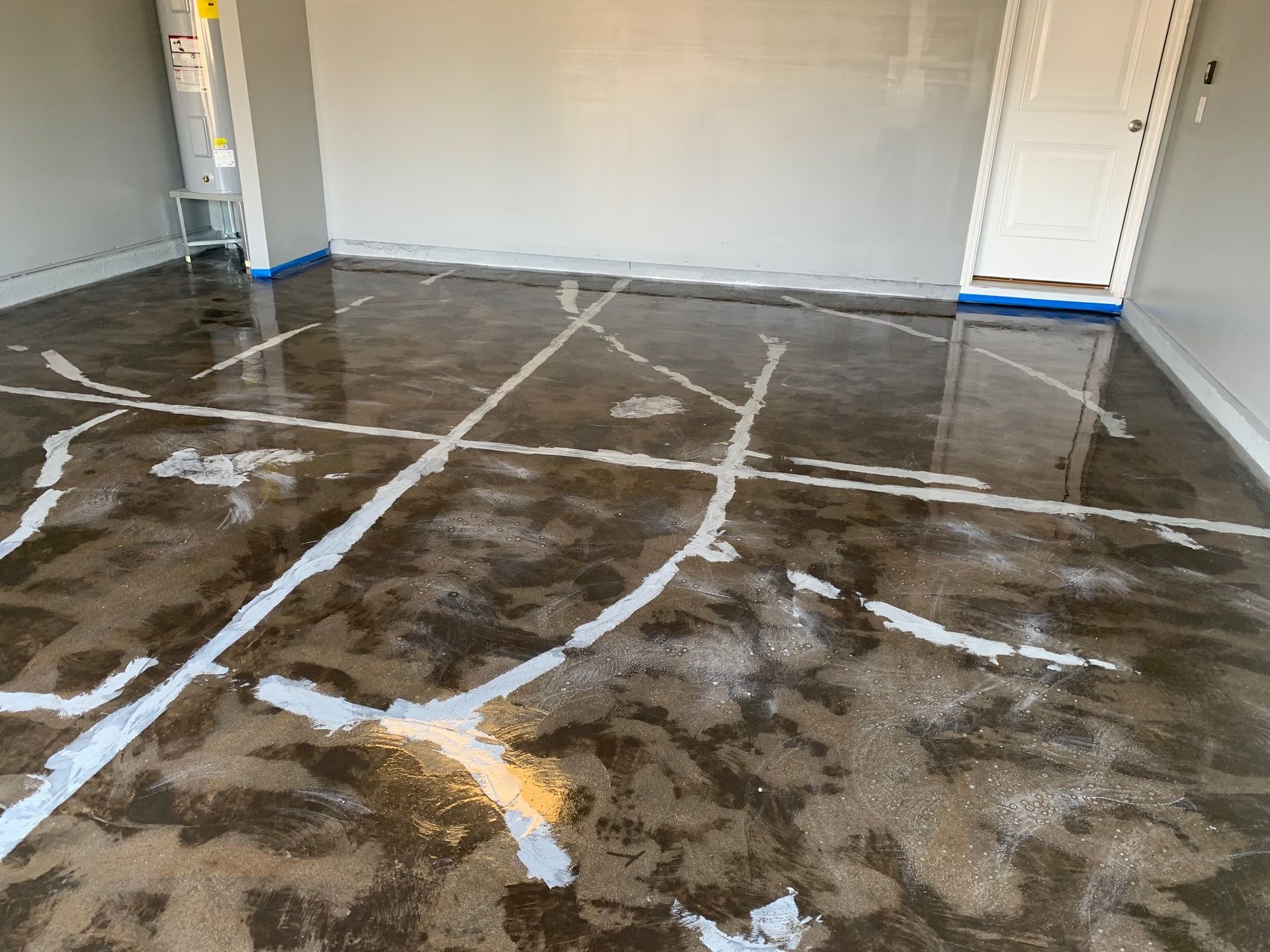 Empty garage with a wet, stained concrete floor and white walls, viewed toward a closed door.