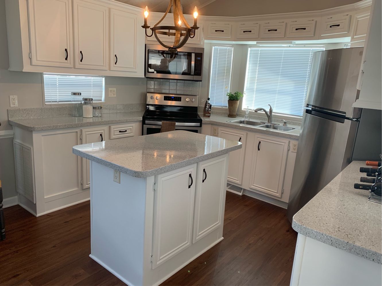 Bright white kitchen with island, stainless steel appliances, wood floor, and bay window seating