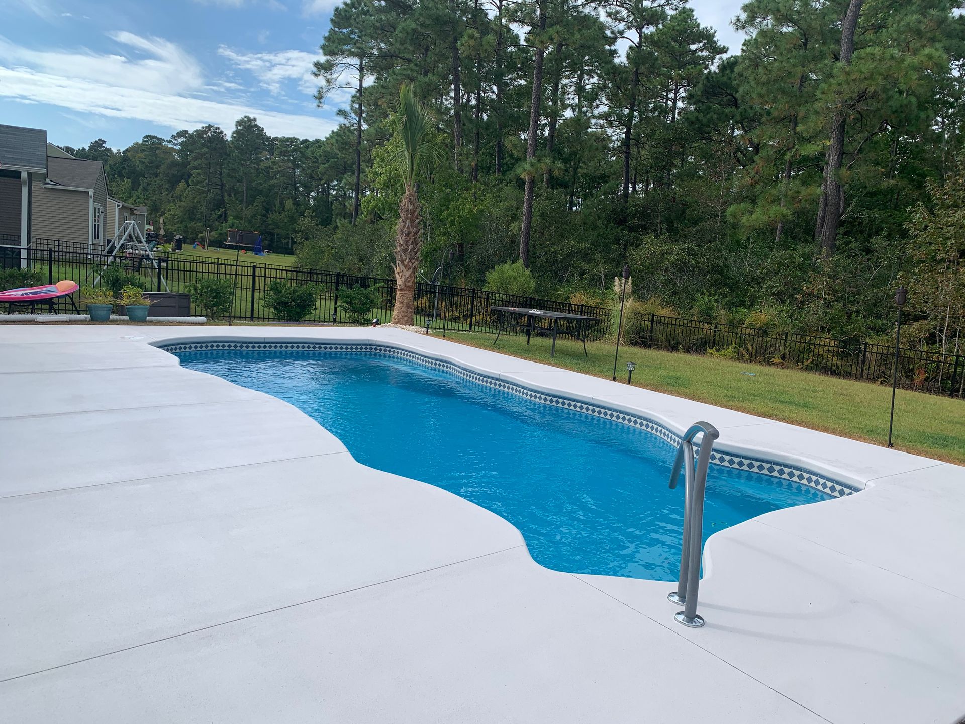 Backyard swimming pool with blue water, white deck, and trees in the background