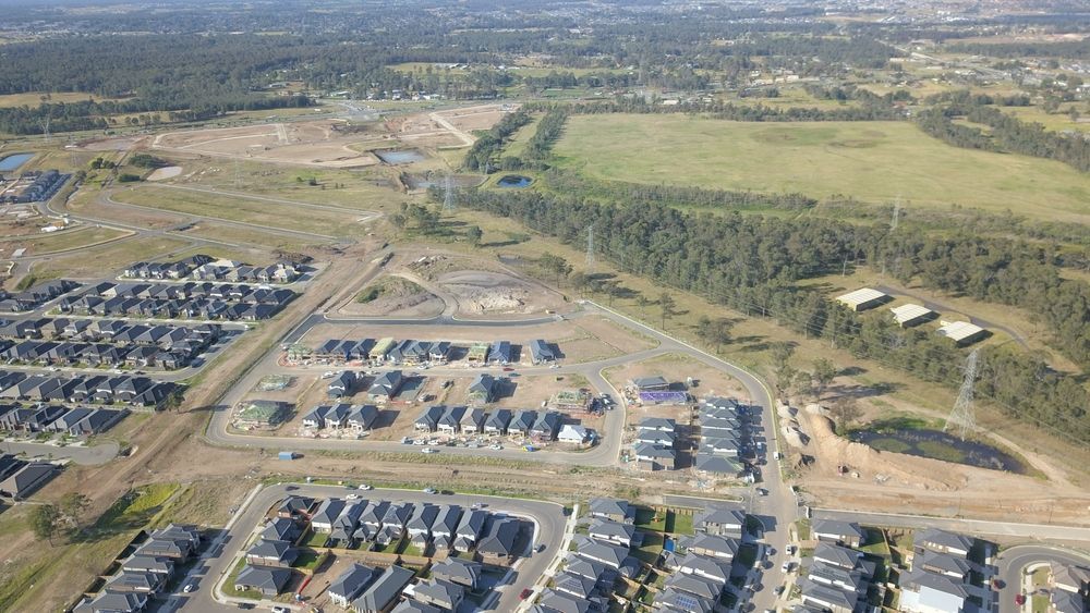 Aerial view of a suburban housing development beside open green fields and dirt roads