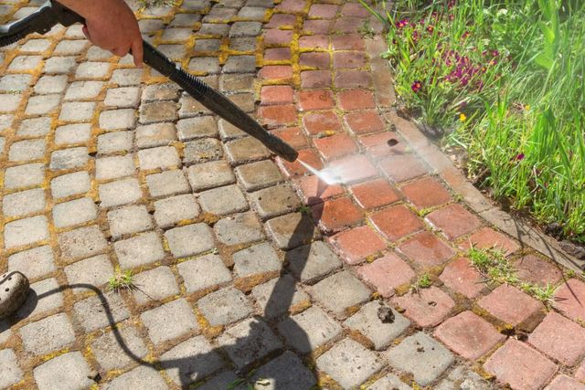 Pressure washing cobblestone and brick pavement beside a flower bed.