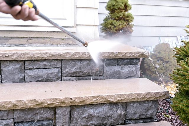 Pressure washing stone steps and retaining wall outside a house