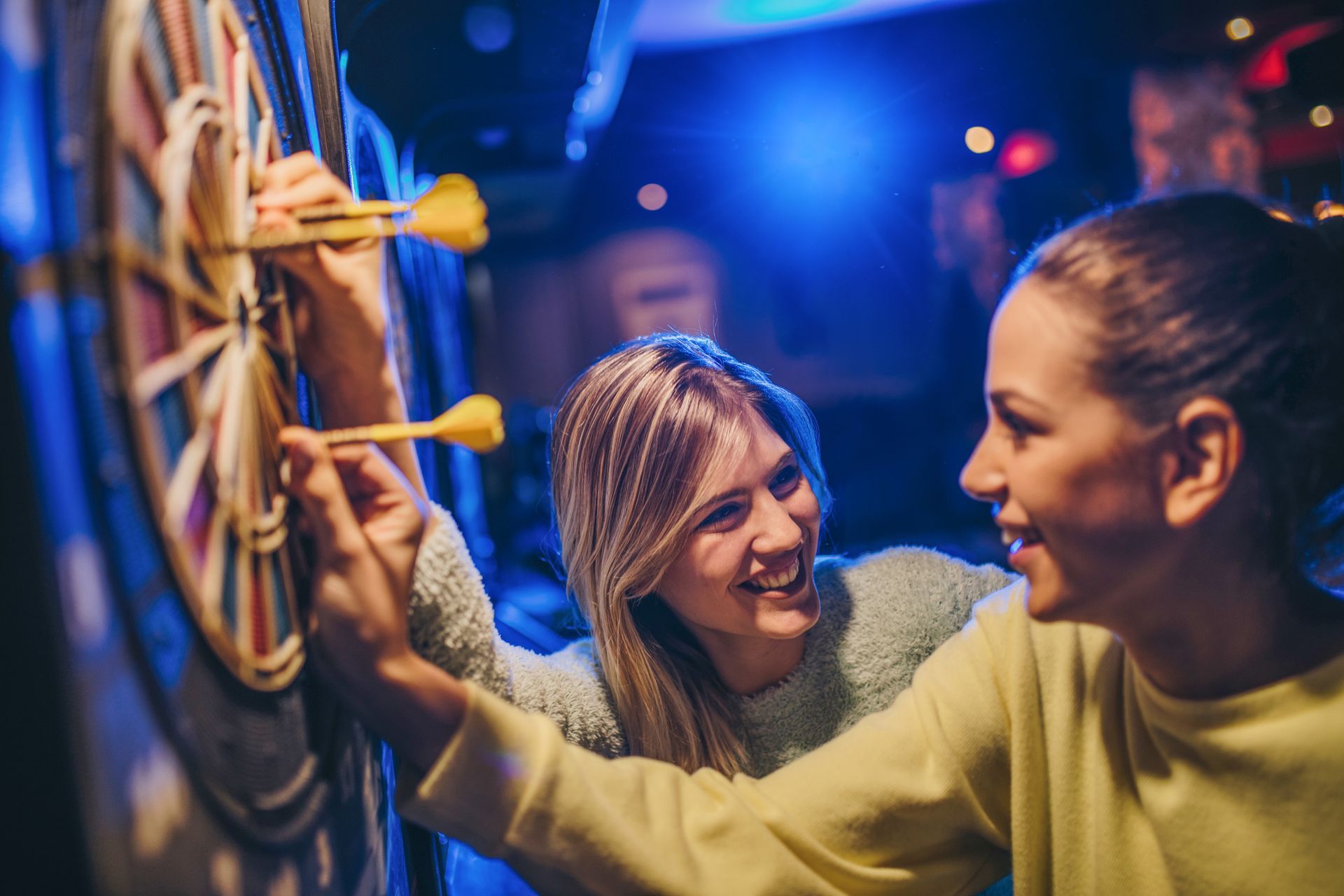 Two women are playing darts together in a bar.