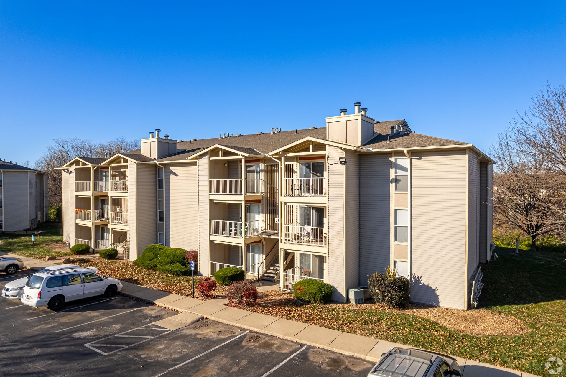 Apartment building with balconies and parking lot under a blue sky.