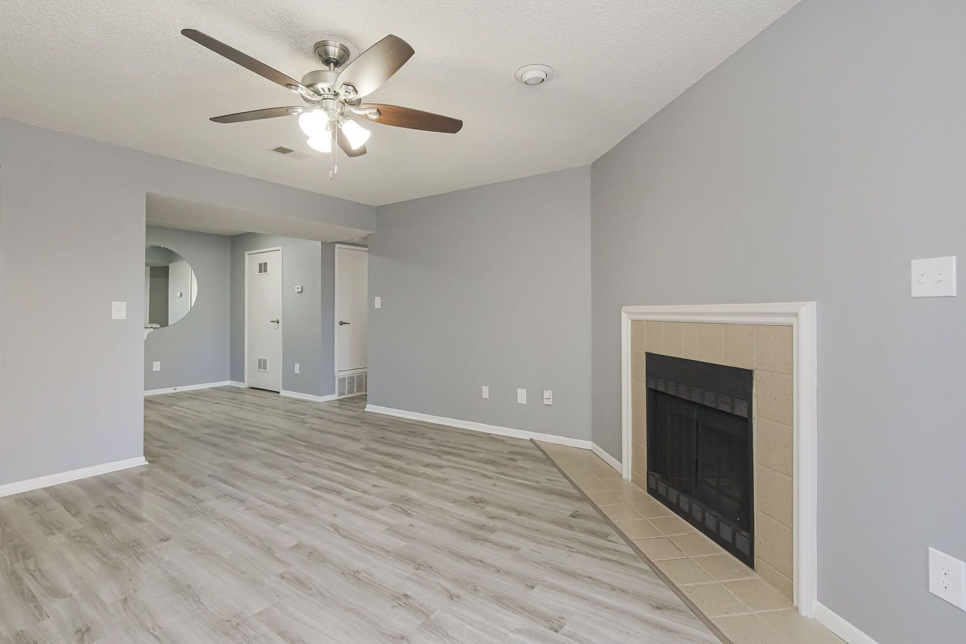 Empty living room with fireplace, ceiling fan, and light gray walls and flooring.