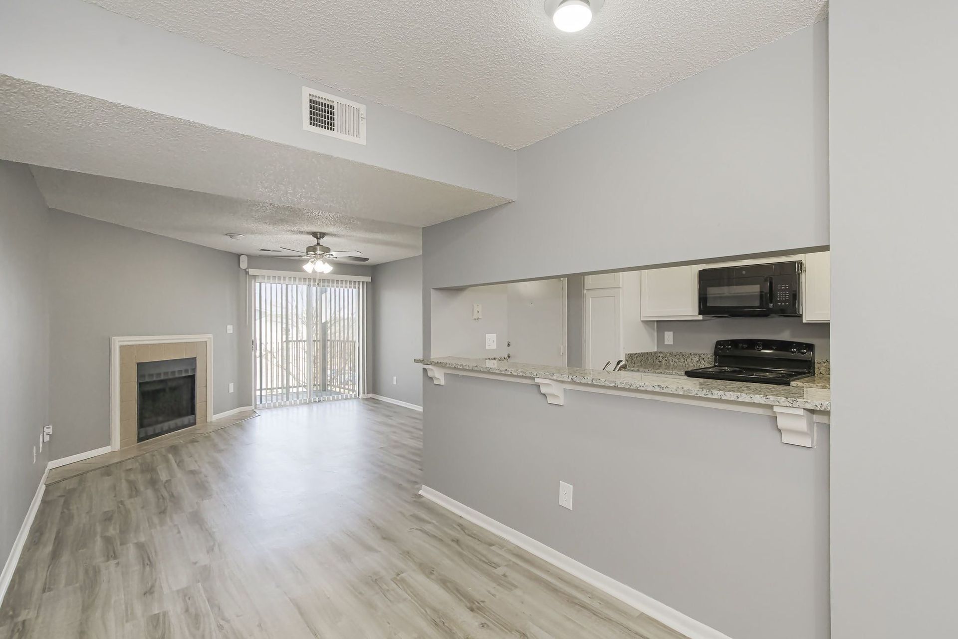 Empty living space with gray walls, a fireplace, and a kitchen area visible through a countertop opening.