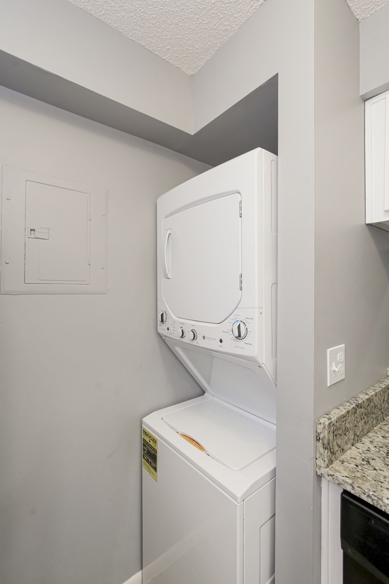 Stacked white washer and dryer in a gray alcove, next to a countertop.