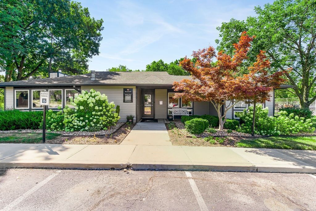 Gray building with a path and landscaping in front; parking lot in foreground.
