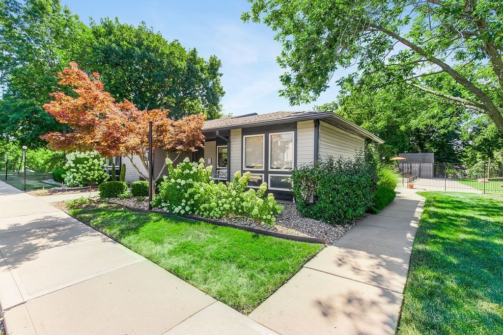 Low-slung, modern home with light-colored exterior, large windows, and lush greenery in front yard.