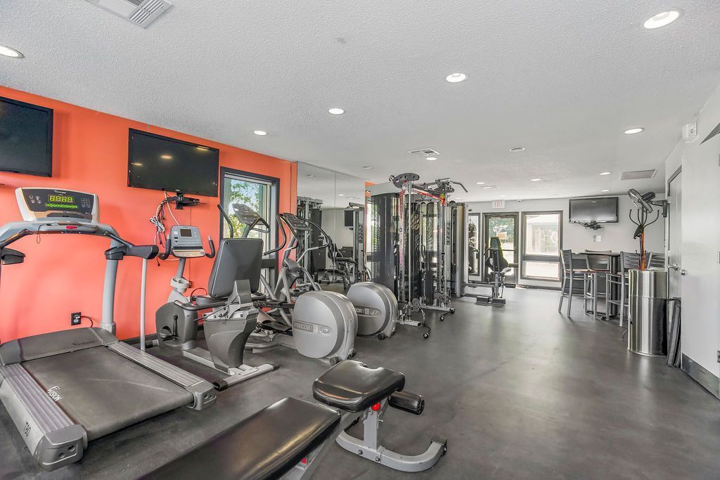 Gym with treadmills, weight machines, and TVs on orange and white walls.