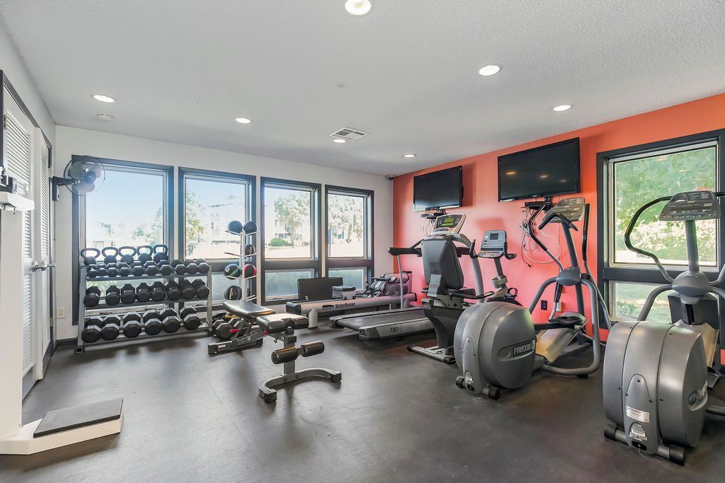Gym with weights, exercise machines, windows, and two TVs on orange wall.