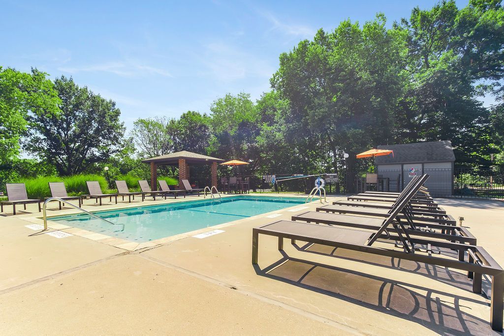 Poolside scene with lounge chairs, blue water, and trees under a sunny sky.