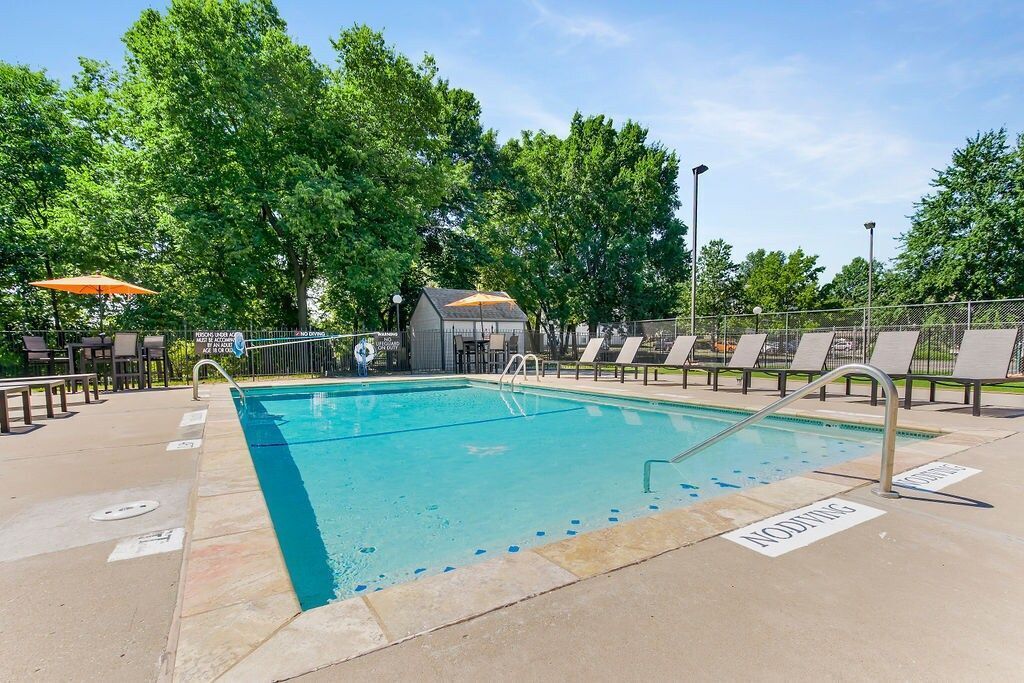 Swimming pool surrounded by lounge chairs, trees, and small cabana on a sunny day.