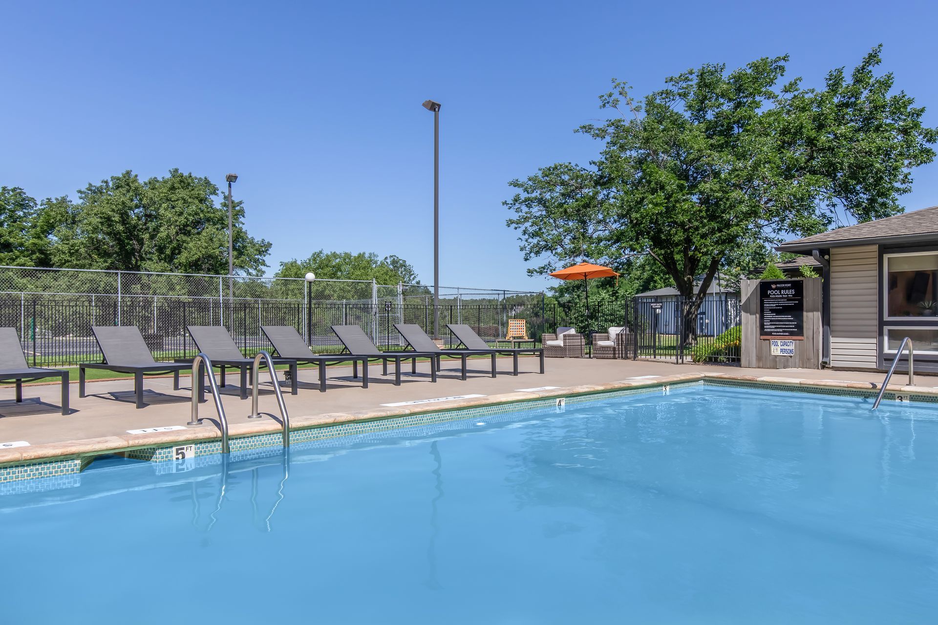 Swimming pool with lounge chairs, trees, and a clear blue sky.