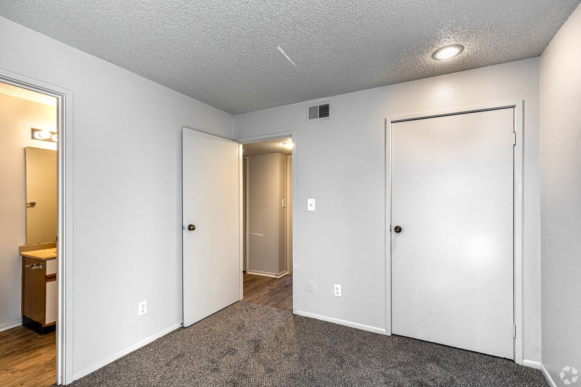 Bedroom with gray walls, doors, and carpet. A door to the bathroom is on the left.