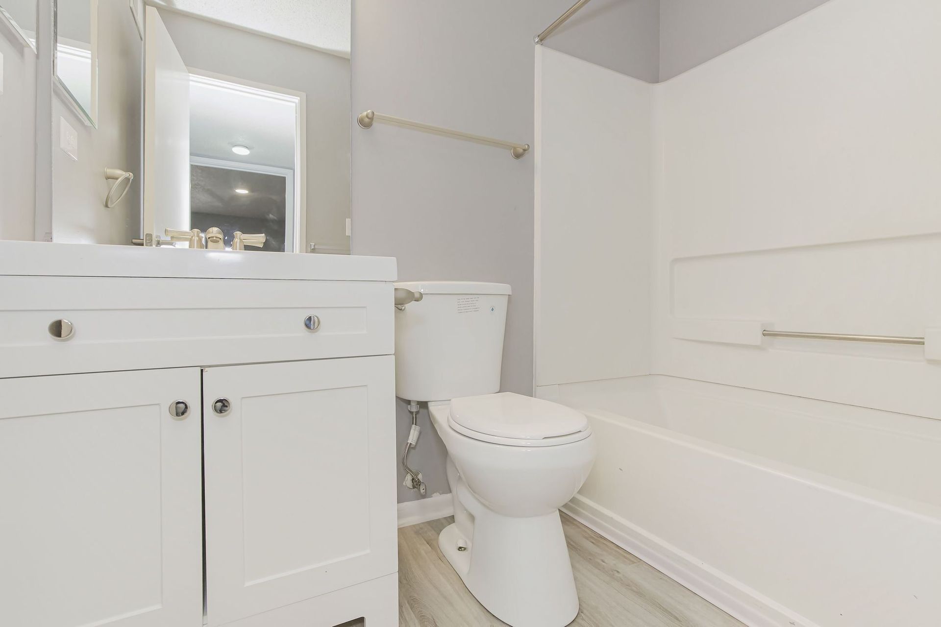 Bathroom with white vanity, toilet, and bathtub; gray walls and light wood-look flooring.