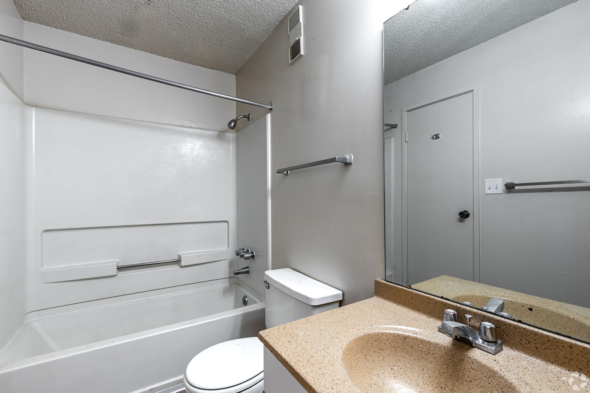 Bathroom with white tub, toilet, and sink with a beige countertop, mirror, and gray walls.