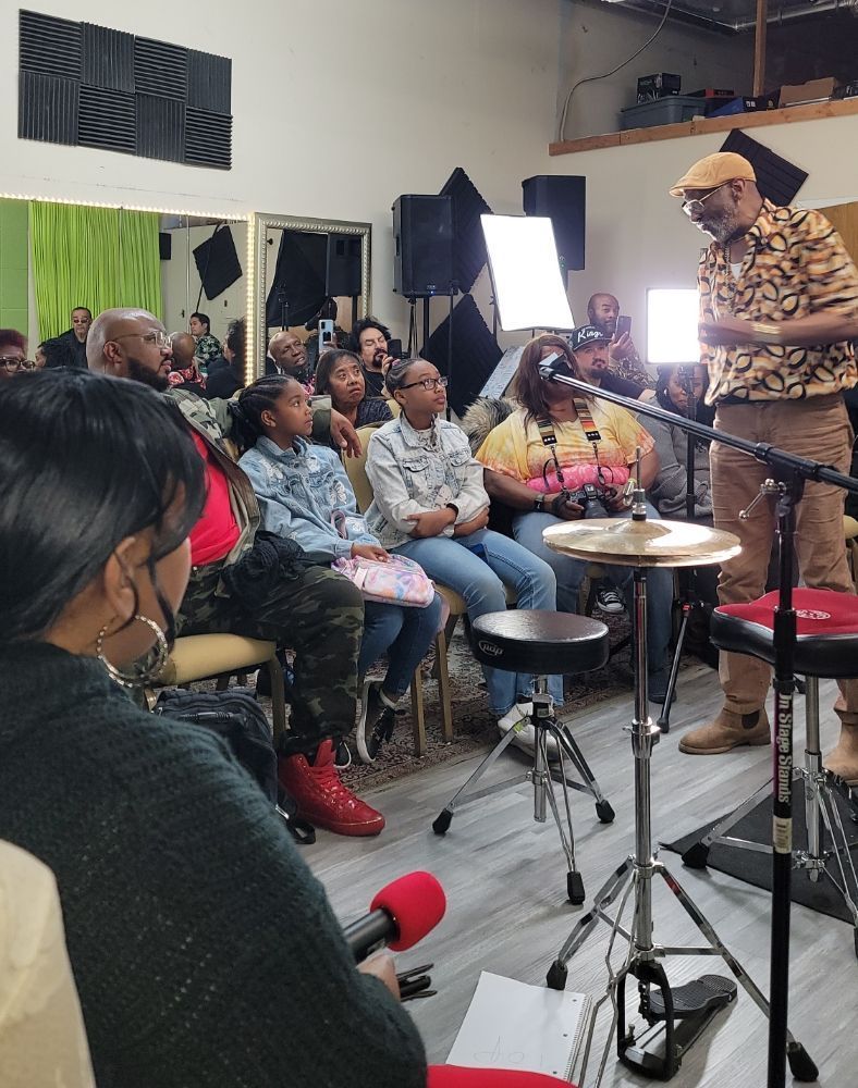 A group of people are sitting in front of a drum set