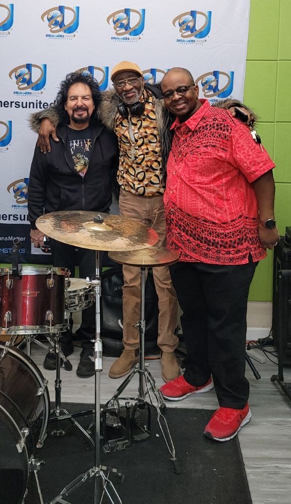 Three men are posing for a picture in front of a drum set.