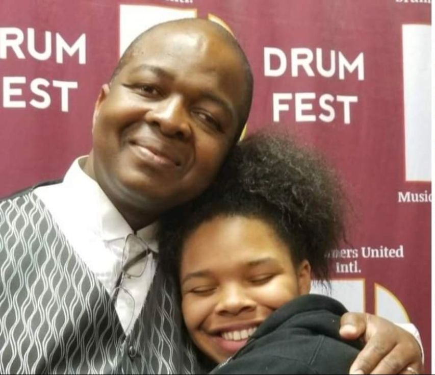 A man and woman are posing for a picture in front of a drum fest banner