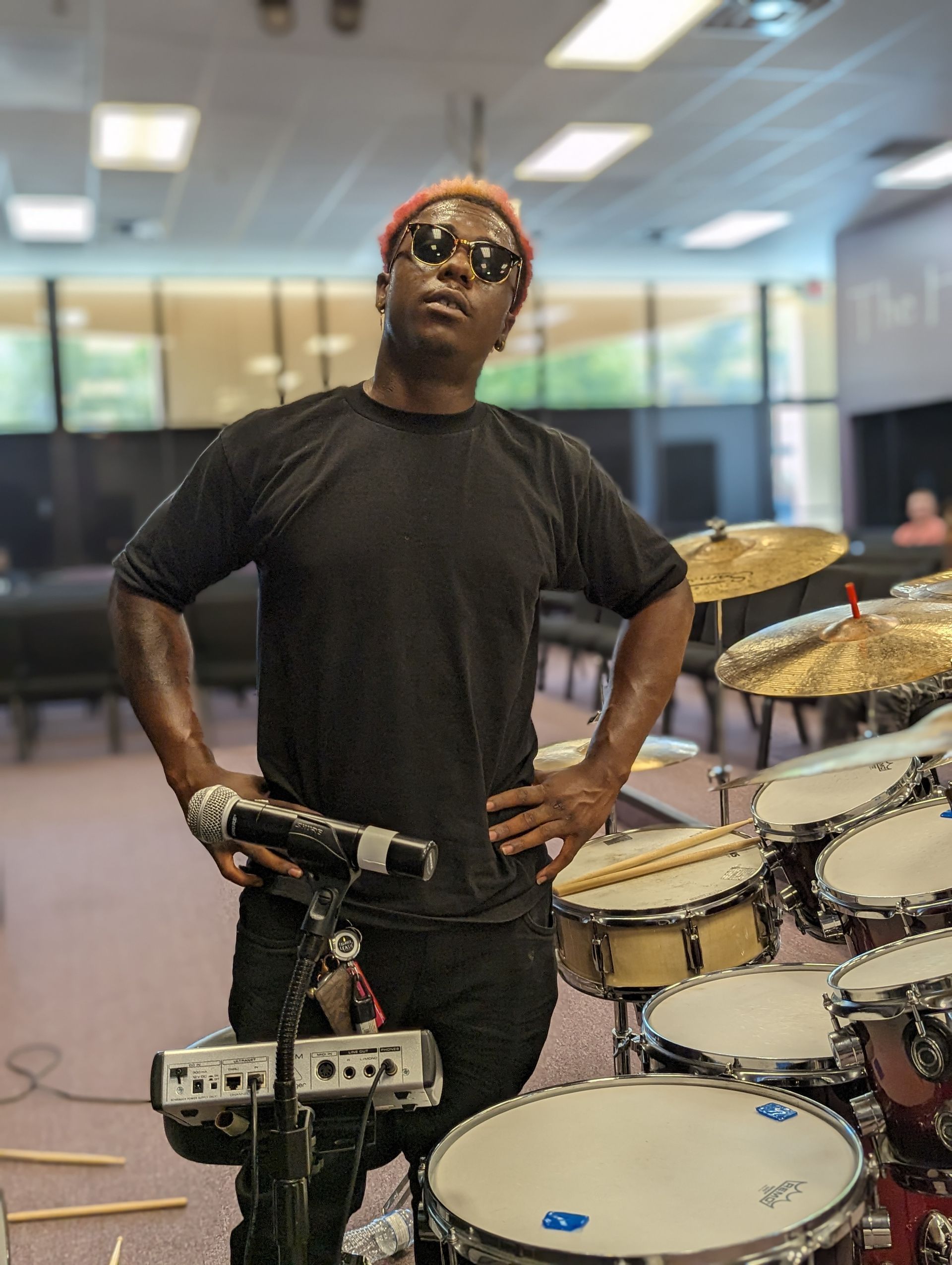 A man wearing sunglasses is standing in front of a drum set.
