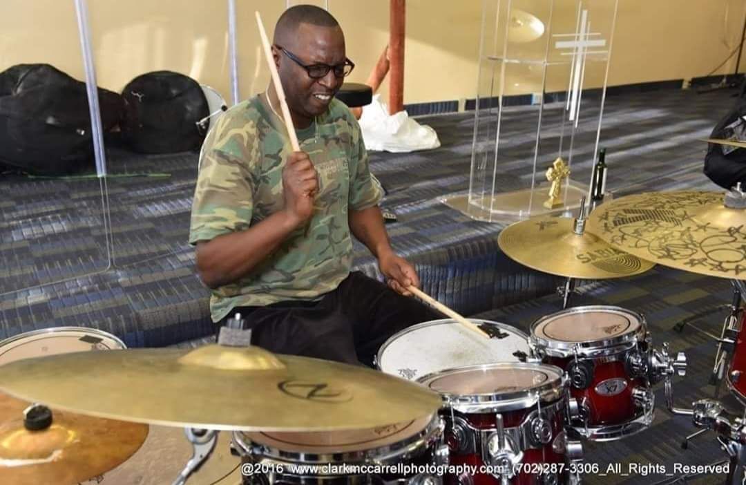 A man is playing drums in a church with a cross in the background.