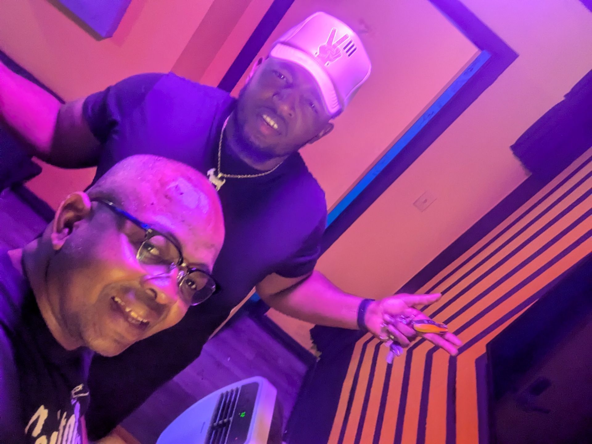 Two men are posing for a picture in a room with purple lights