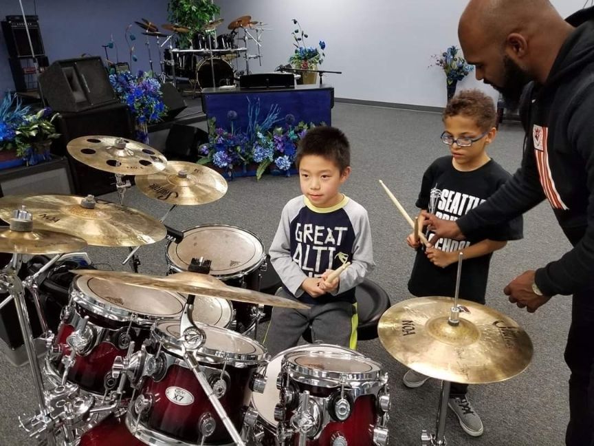 A man is teaching two young boys how to play drums