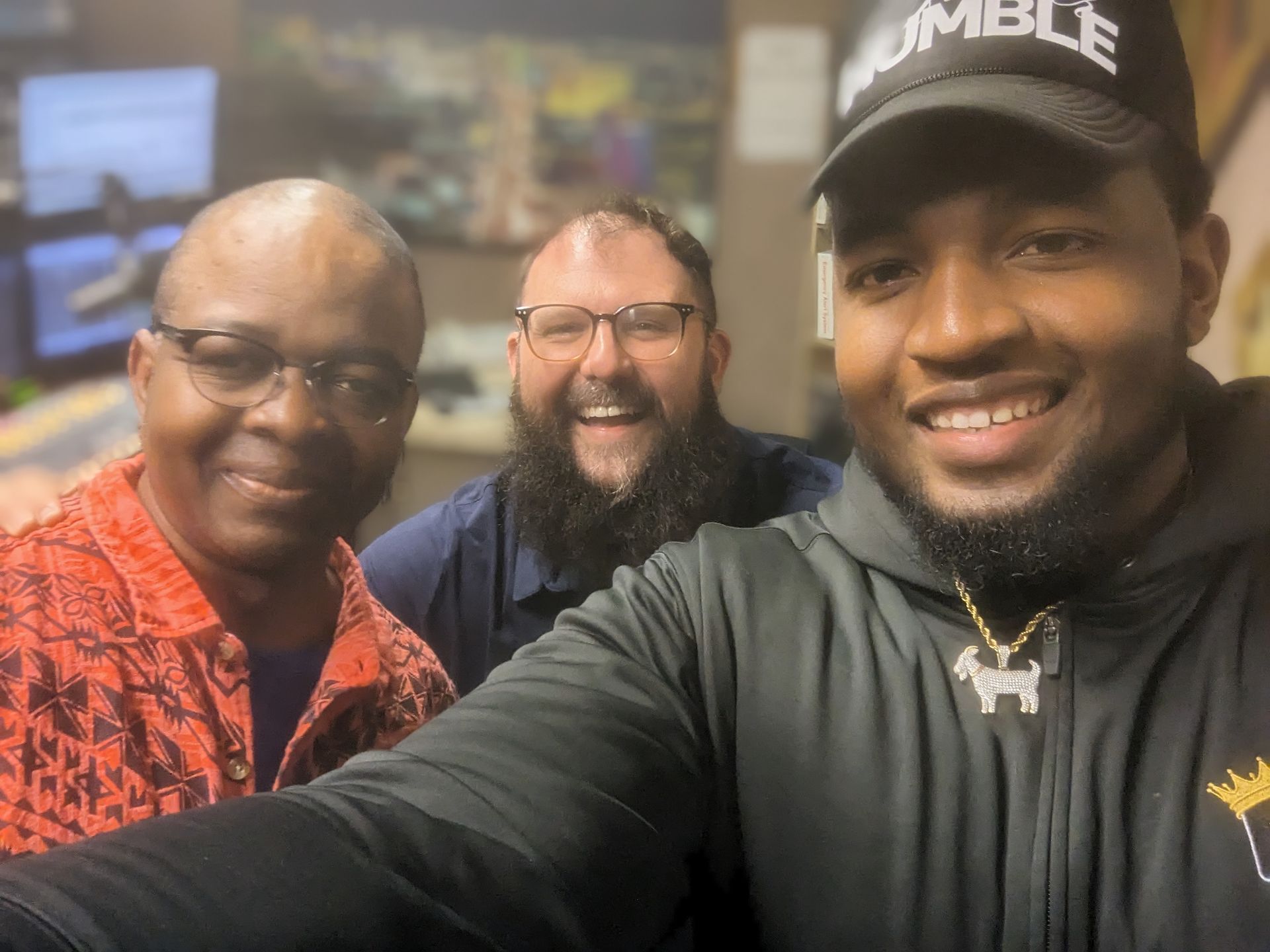 Three men are posing for a picture and one of them is wearing a hat that says rumble