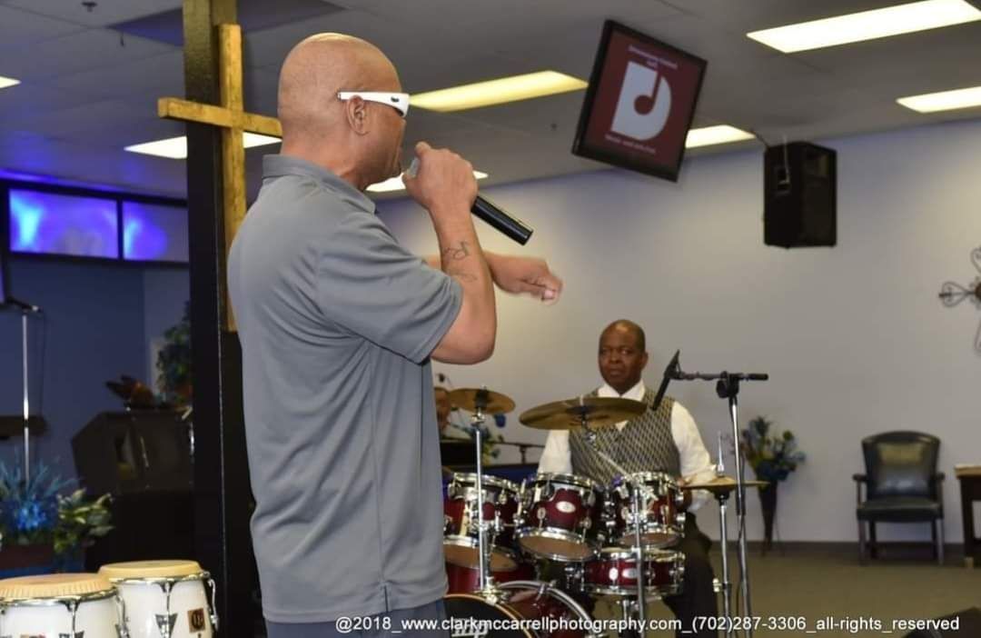 A man singing into a microphone in front of a drum set