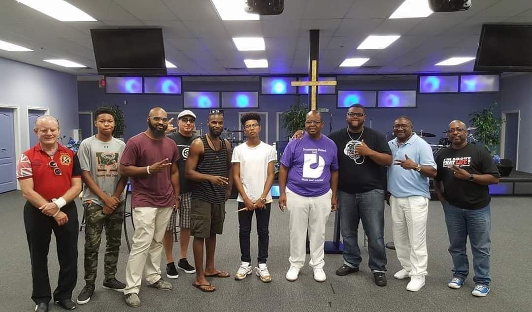 A group of men are posing for a picture in a room with a cross in the background.