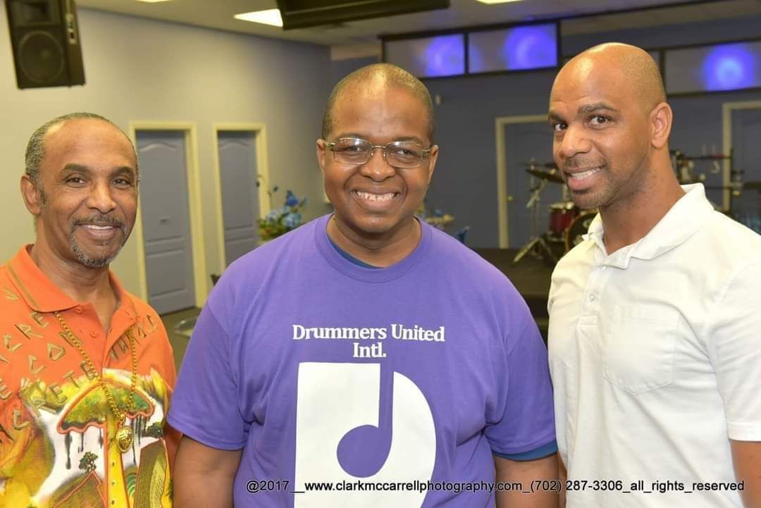 Three men are posing for a picture and one of them is wearing a drummers united shirt